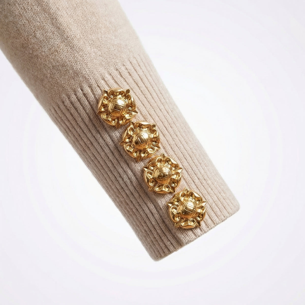 Gold earrings on a beige sweater sleeve