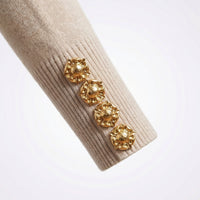 Gold earrings on a beige sweater sleeve