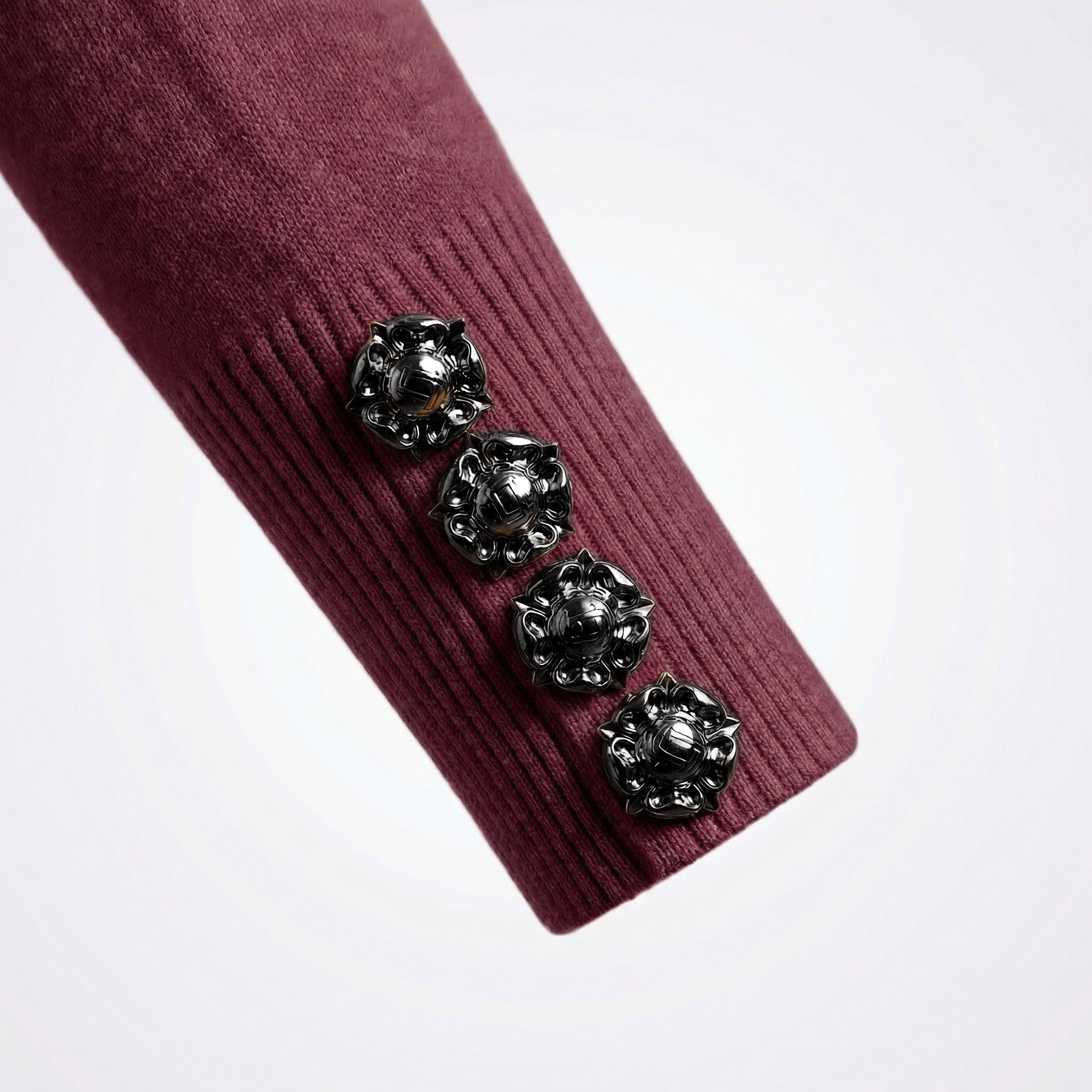 Close-up of a maroon ribbed fabric with decorative black buttons on a white background