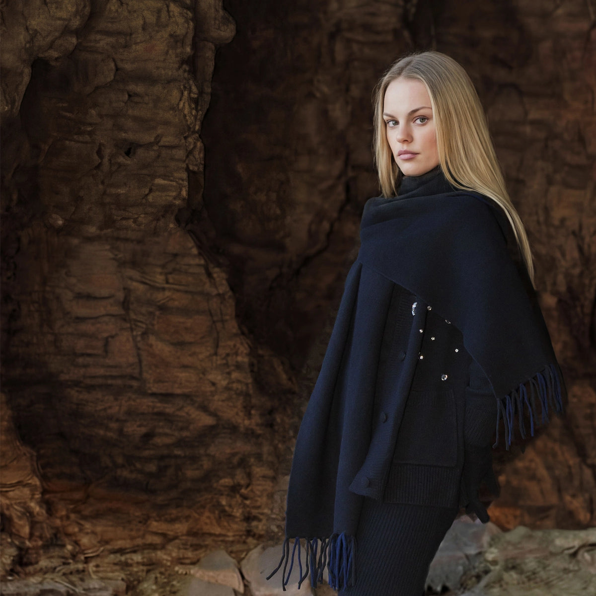 Woman wearing a dark blue poncho with fringe standing against a rocky background